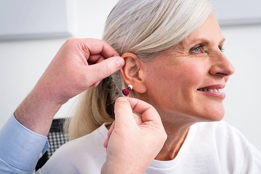 Ältere Frau lässt sich von einem Hörakustiker ein modernes Hörgerät ins Ohr einsetzen.